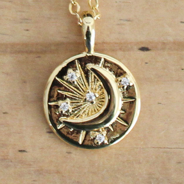 Gold celestial coin necklace featuring a crescent moon, sparkling crystal accents and starburst design