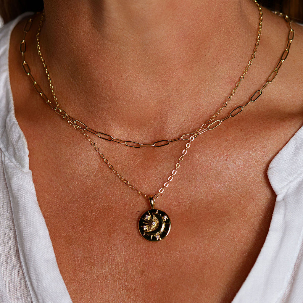 Woman wearing a gold celestial moon coin necklace layered with a gold paperclip chain