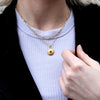 Gold evil eye pendant necklace with a sapphire as the eye. Show with a paperclip necklace that layers great with the evil eye necklace. Margie Edwards Designs designs. Shown with a black velvet jacket and white tee.  